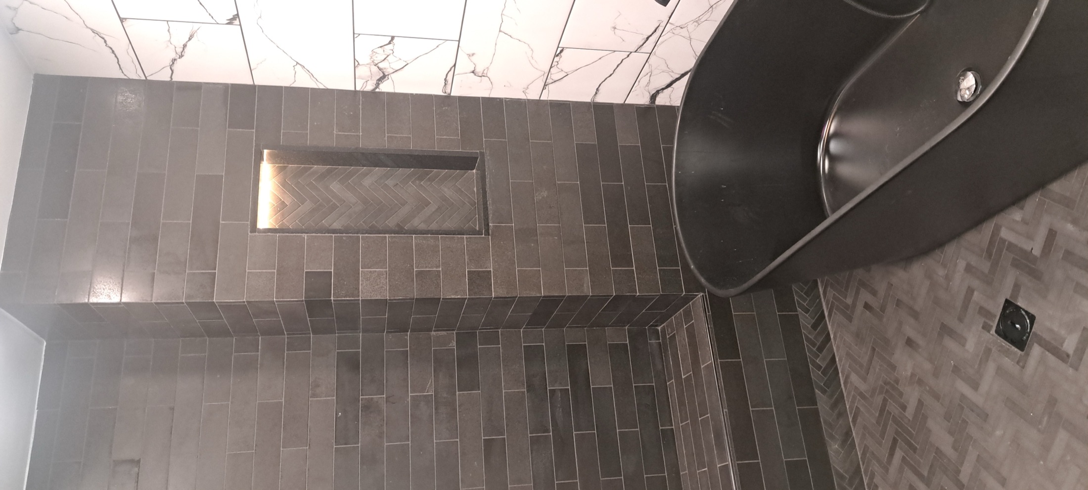 Dark tile shower wall with recessed niche and black tub fixture