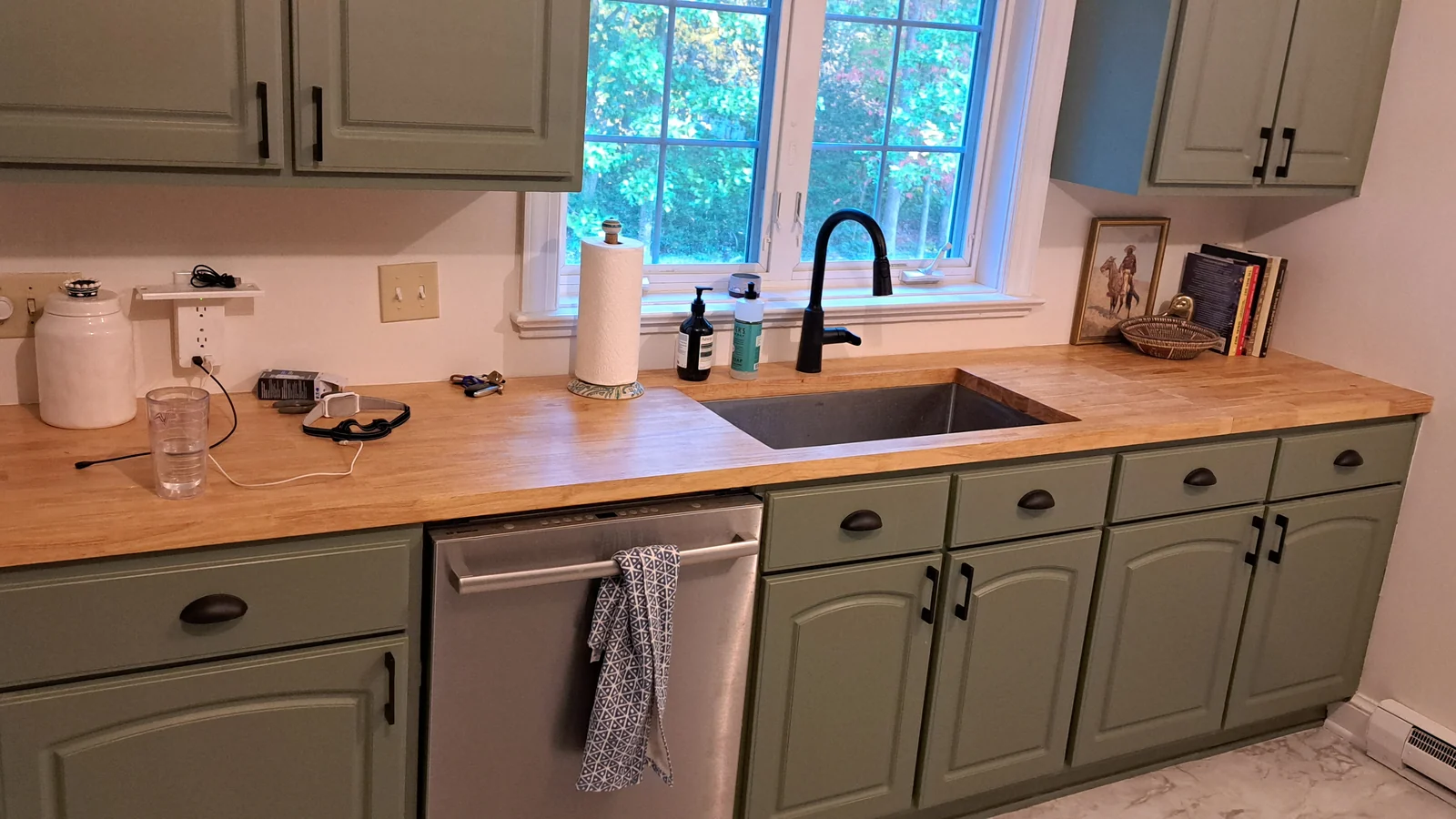 Finished kitchen remodel with green cabinetry, butcher block countertops, and a black sink fixture